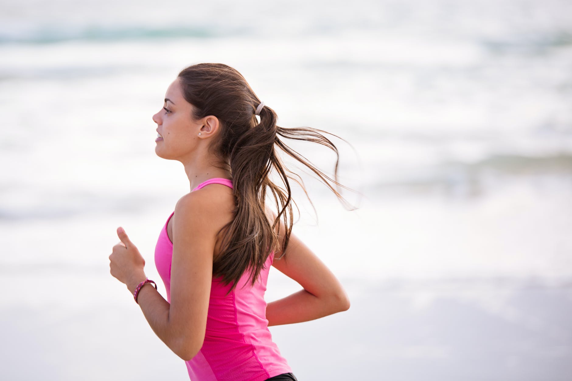 A woman in a pink tank top running on the beach, engaging in exercise after weight loss surgery.