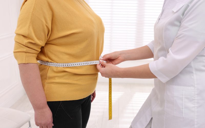 Woman measuring waist with tape measure, part of bariatric treatments for weight loss.