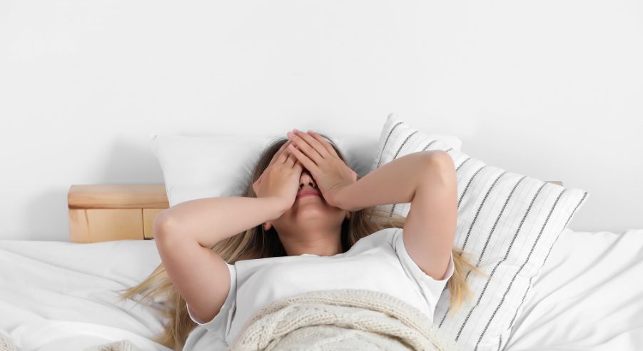 A woman in bed, hands covering her eyes, possibly experiencing discomfort or pain due to reflux after bariatric surgery.