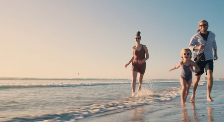 A family joyfully runs on the beach at sunset, their silhouettes against the vibrant sky.